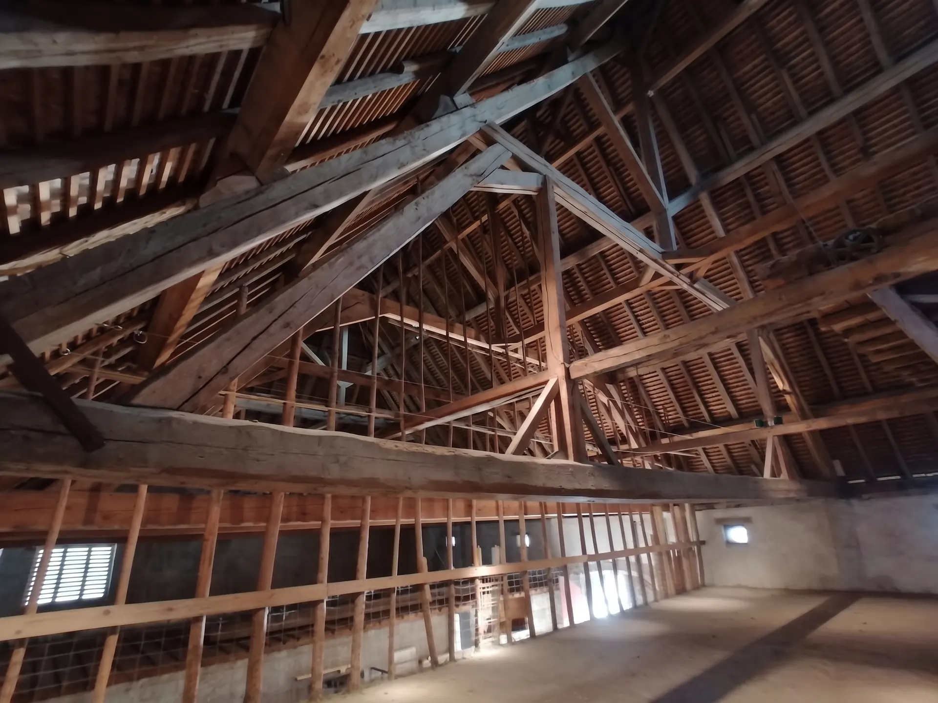 La charpente de bois sous le toit&nbsp;: de grandes fermes et des entraits apparents au-dessus d'un plancher bordé d'une barrière de bois